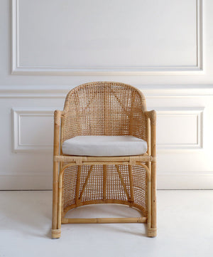 Woven chair with a white cushion against a light-colored wall.
