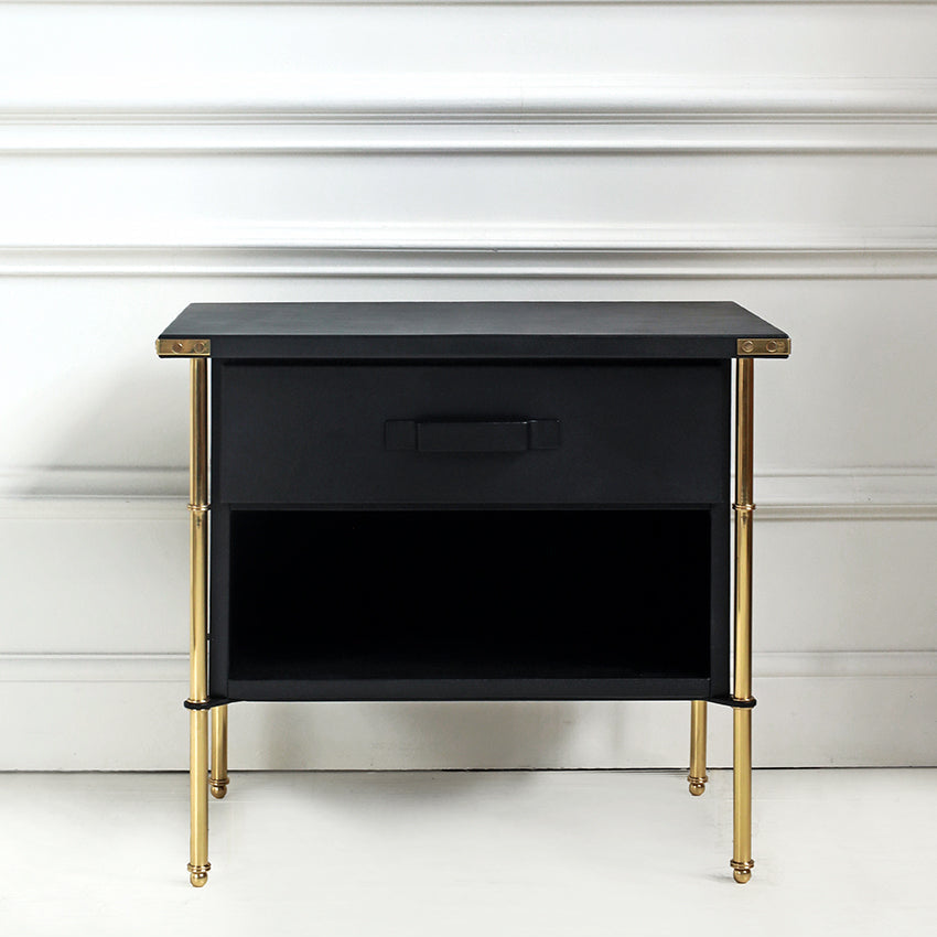 Black nightstand with gold legs against a white wall