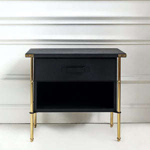Black nightstand with gold legs against a white wall
