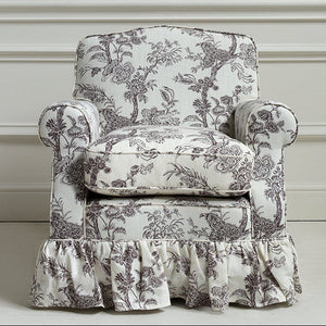 A classic upholstered armchair with a ruffled skirt base, featuring a black and white toile de Jouy pattern, set against a white paneled wall.