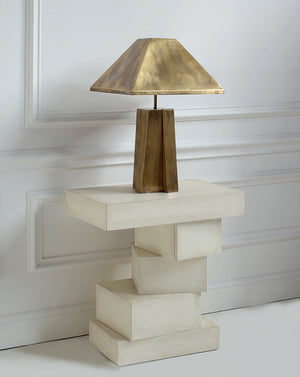 Table lamp with a gold shade on a white pedestal against a white wall.