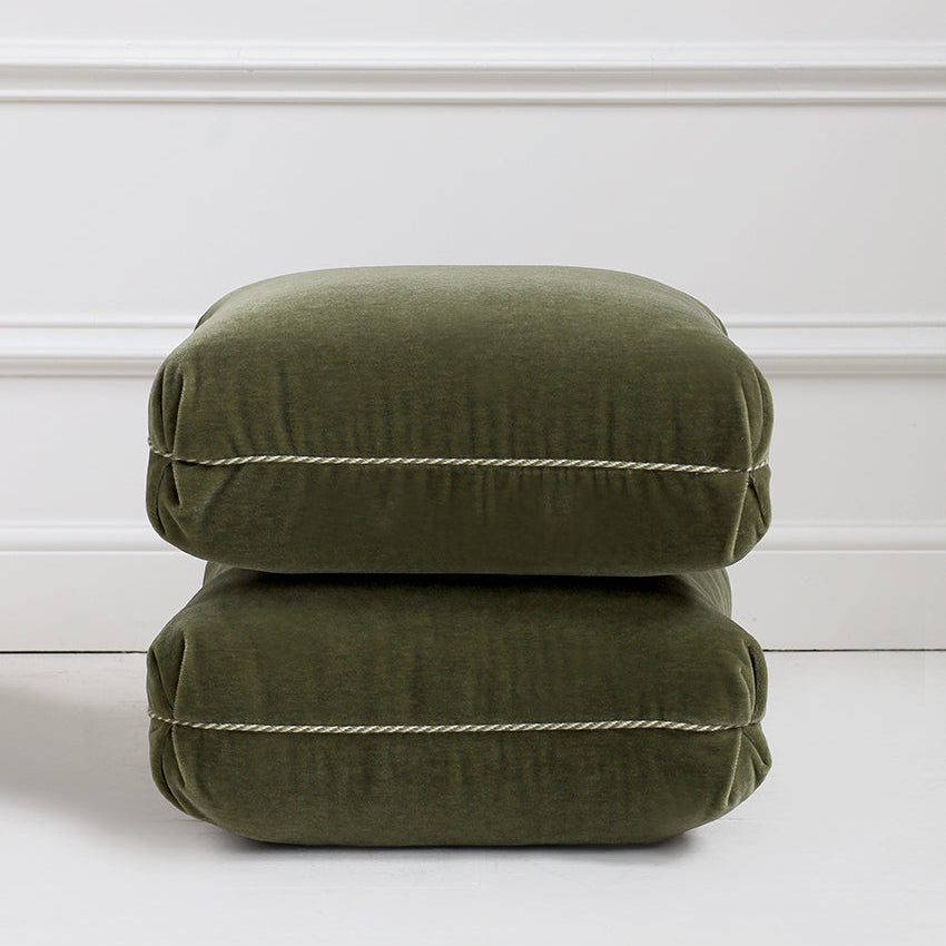 Two stacked green cushions on a white floor with a white wall background
