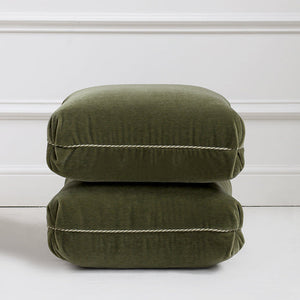Two stacked green cushions on a white floor with a white wall background