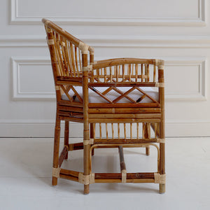 Rattan chair with a white cushion against a white paneled wall.