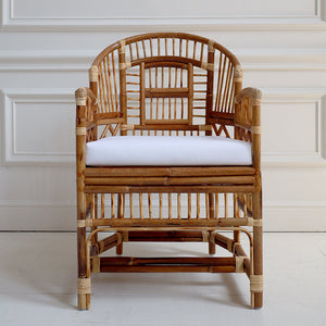 Rattan chair with a white cushion against a white paneled wall.